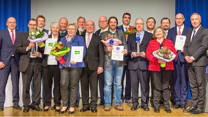 A group of people holding awards and flowers standing on a stage