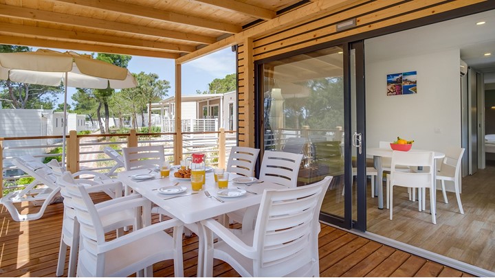 Essbereich im Freien mit weißen Stühlen und einem für das Frühstück gedeckten Tisch auf einem Holzdeck