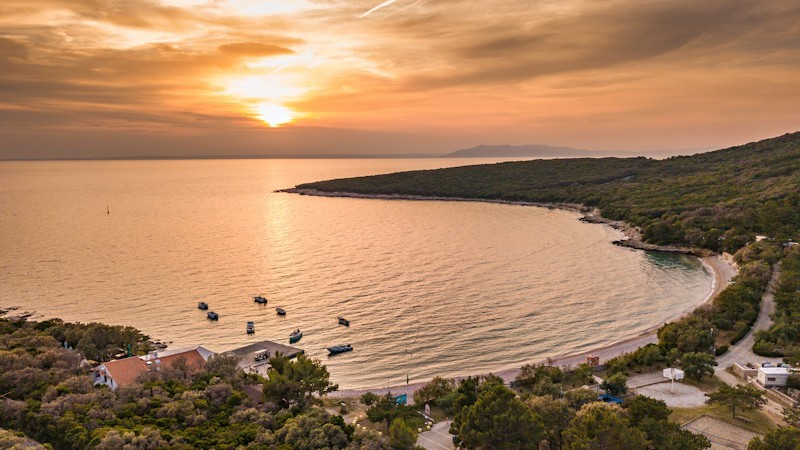 A beautiful sunset over a bay with small boats and a coastal landscape on Cres