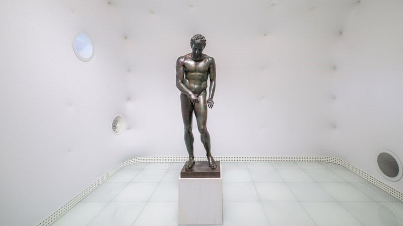 Ancient bronze statue displayed in a modern white room
